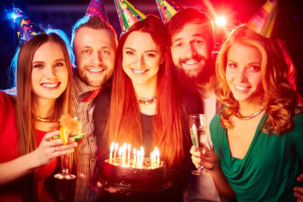 Group of happy friends in birthday caps looking at camera